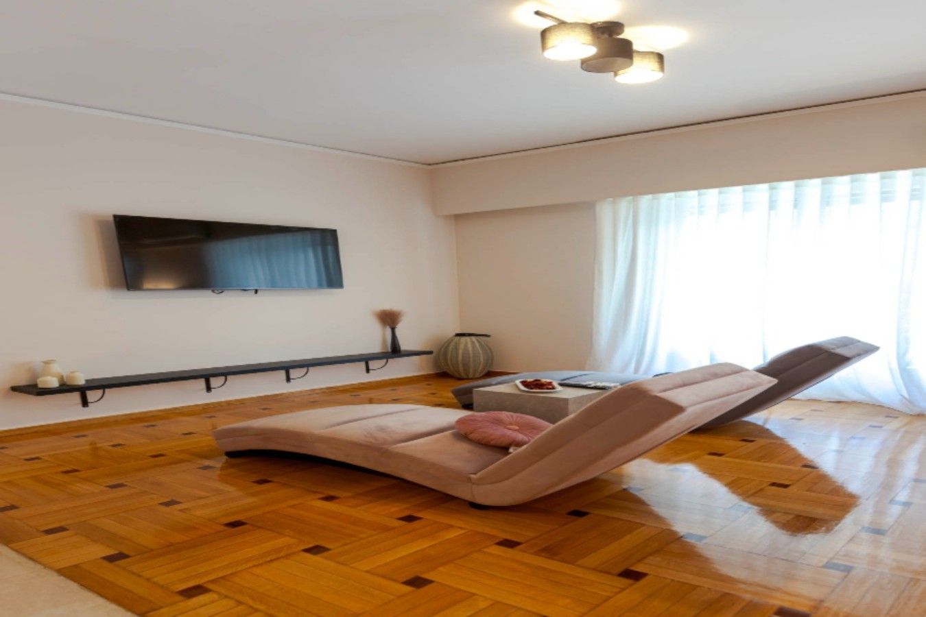 Un salon moderne avec un parquet en bois, un fauteuil inclinable, un téléviseur à écran plat fixé au mur et une petite table d’appoint sur laquelle se trouvent un vase et un bol.