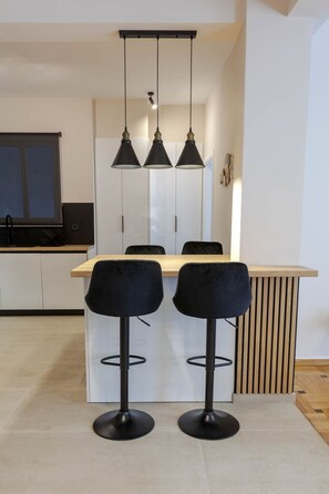 Een moderne keuken met een houten aanrecht, twee zwarte barkrukken en hanglampen.