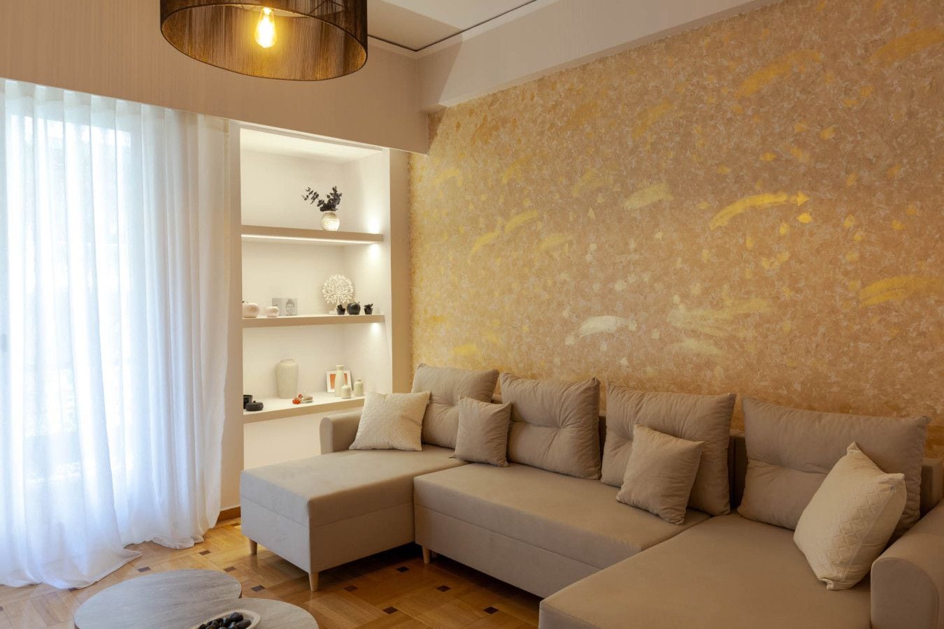 Una sala moderna con un sofá seccional, una estantería empotrada y una pared grande con textura.