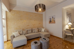 Een moderne woonkamer met een modulaire bank, twee ronde houten tafels, een hanglamp en kunstwerken aan de muur.