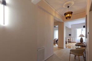 A spacious living area with a high ceiling, a modern pendant light, and a view into another room with a dining table and chairs.