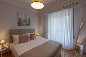 Een hotelkamer met een bed, een nachtkastje met een lamp, een schilderij aan de muur en een groot raam met gordijnen.