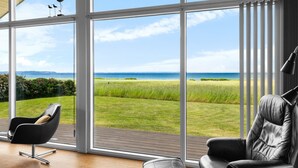 Ein modernes Interieur mit großen Fenstern, die Blick auf ein grünes Feld und das Meer bieten.