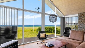 Ein großzügiges Wohnzimmer mit einer großen Glaswand, das Meer und ein grünes Feld bietet.