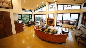 A spacious living area with a curved sofa, multiple seating options, and large windows offering views of the outdoors. - Par-X - Villa Sukoon - 3BHK Valley View (Mahabaleshwar)
