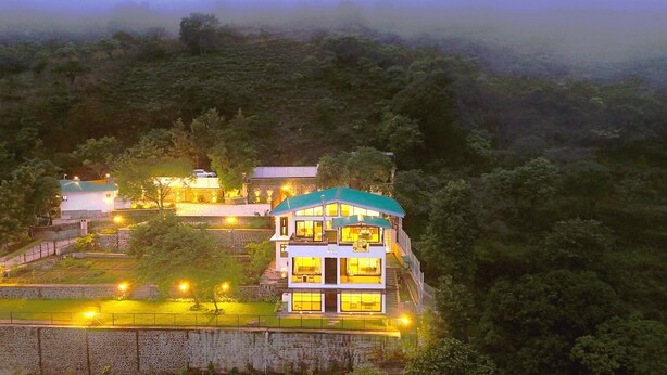 A multi-story building with a green roof, surrounded by lush greenery and a stone wall. - Par-X - Villa Sukoon - 3BHK Valley View (Mahabaleshwar)