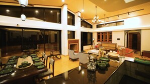A spacious dining area with a long table set for a meal, a fireplace, and a seating area with chairs. - Par-X - Villa Sukoon - 3BHK Valley View (Mahabaleshwar)