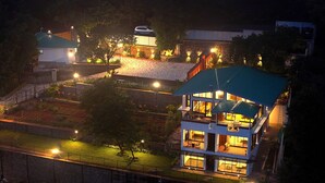 A multi-story house with a green roof, multiple balconies, and a well-lit interior. - Par-X - Villa Sukoon - 3BHK Valley View (Mahabaleshwar)