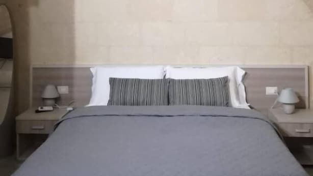 Una habitació amb un llit, dues taules de nit i un sostre de pedra ample i arquejat.