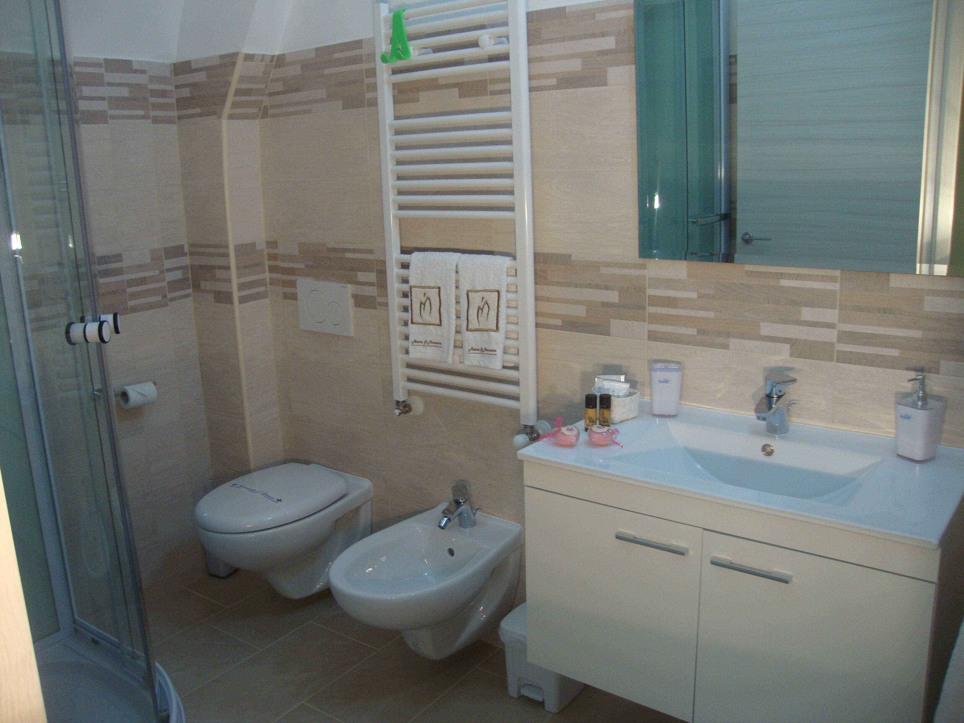 Une salle de bain avec une douche à parois de verre, des toilettes, un bidet et un lavabo avec un miroir au-dessus.