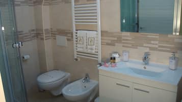 Un baño con cabina de ducha de vidrio, inodoro, bidé y lavamanos con espejo superior.