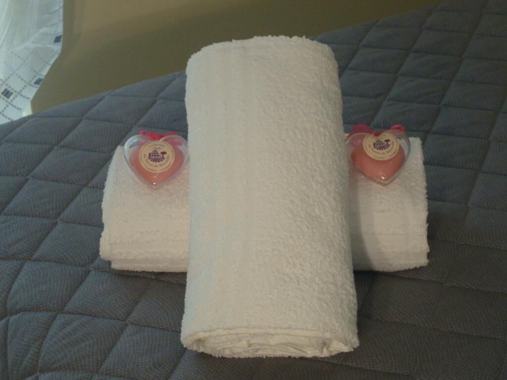 A bed with a quilted gray cover and two rolled white towels with heart-shaped tags on the side.