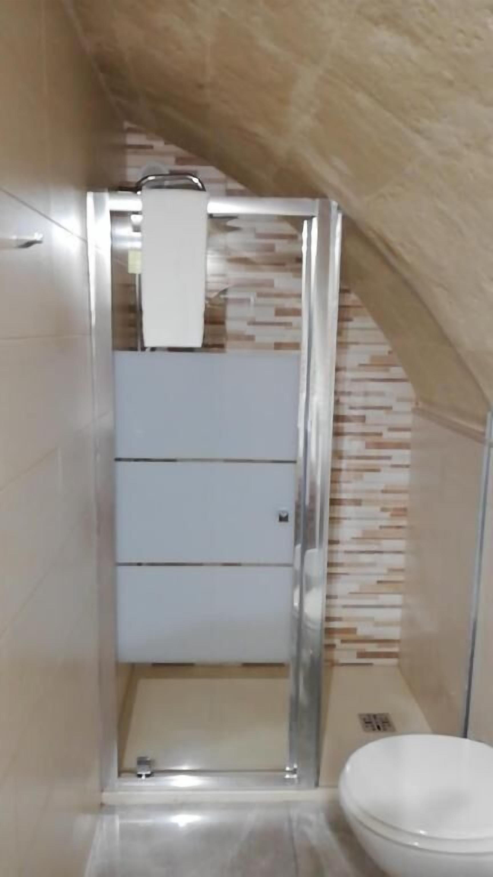 A small, enclosed bathroom with a toilet, a sink, and a shower area.