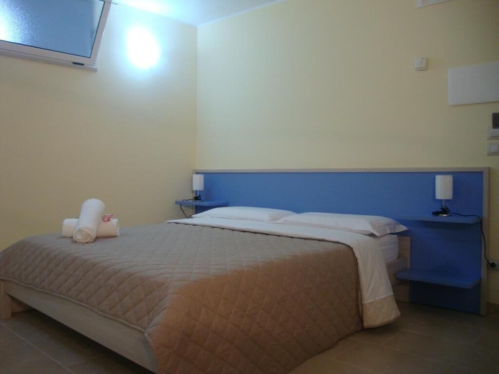 A hotel room with a large bed, two bedside tables, a TV mounted on the wall, and a blue accent wall.