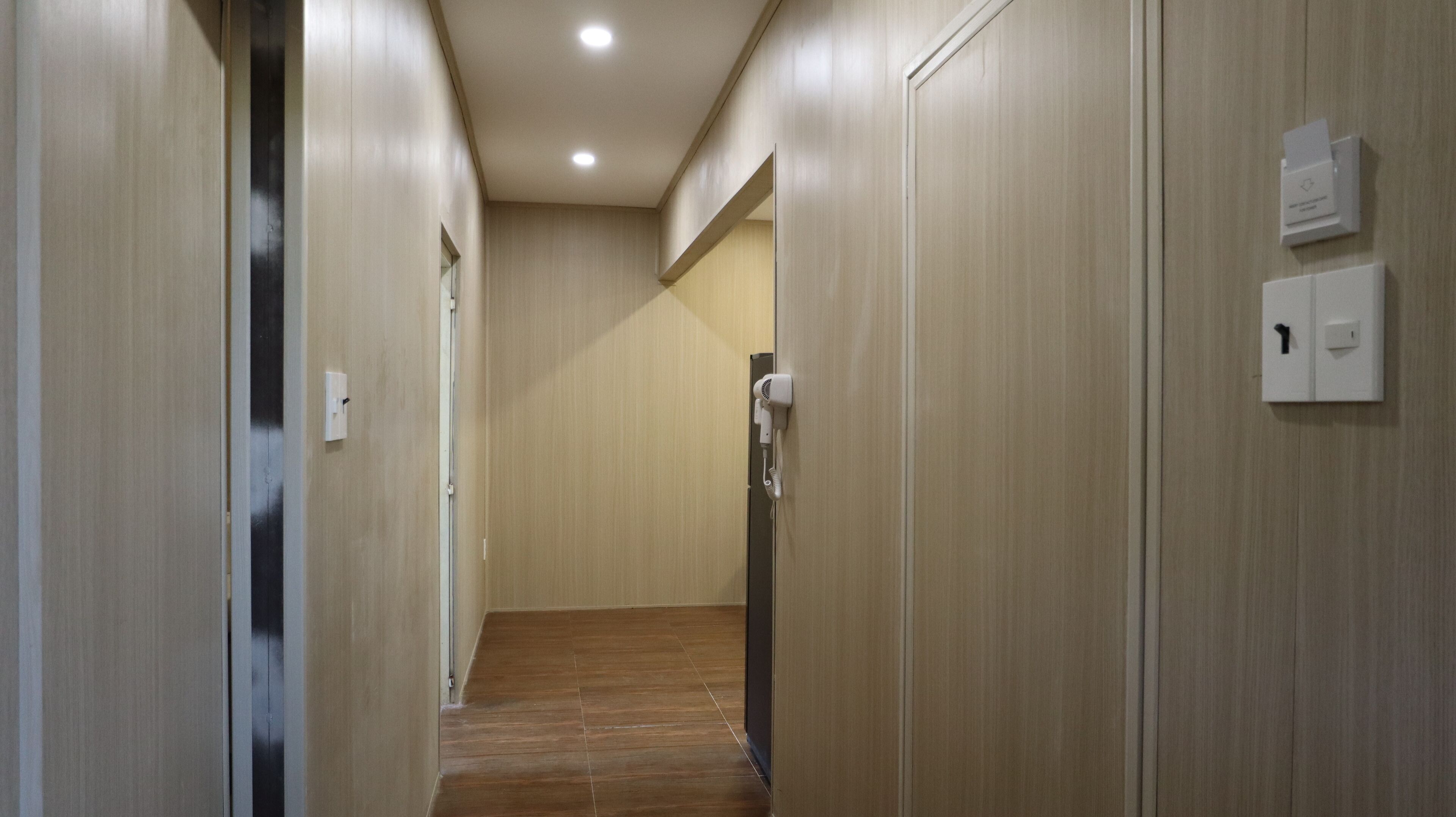 A hallway with wooden walls and a wooden floor, leading to a door with a mirror and a hairdryer on a wall-mounted stand.