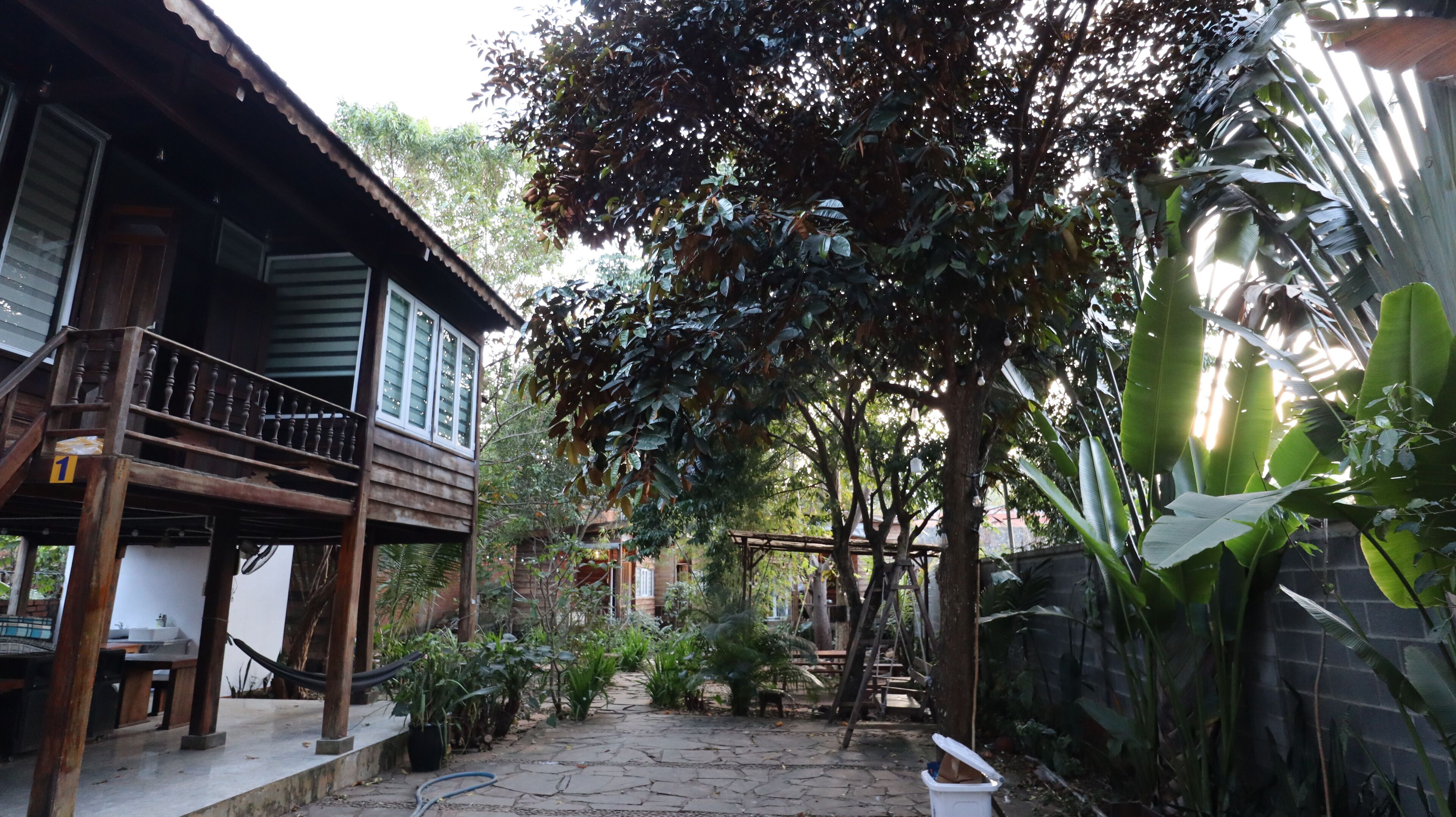 Una casa de madera con balcón, rodeada de abundante vegetación y un sendero de piedra.