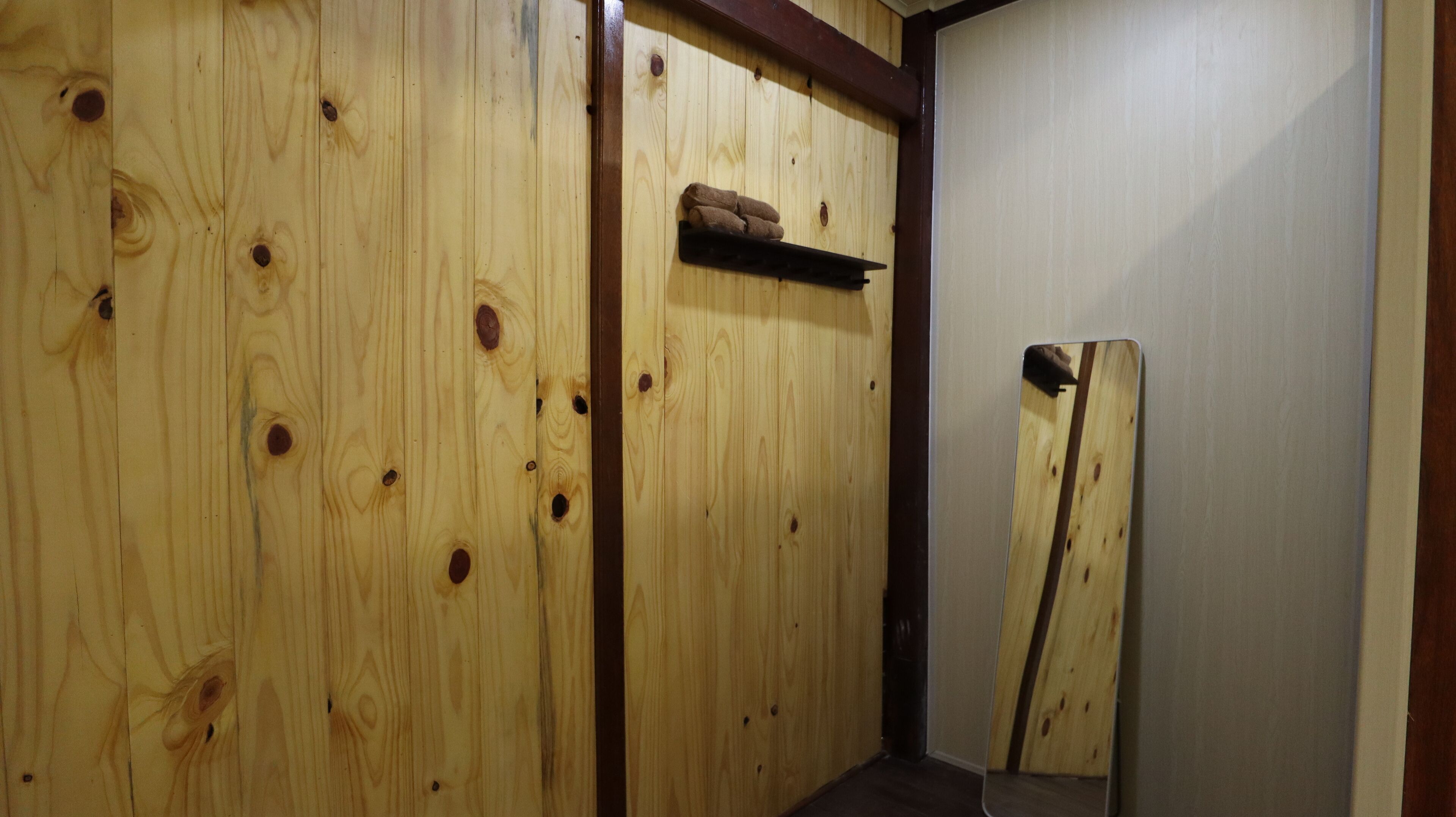 Een houten kamer met een plank waarop handdoeken liggen en een spiegel die de houten wand weerspiegelt.