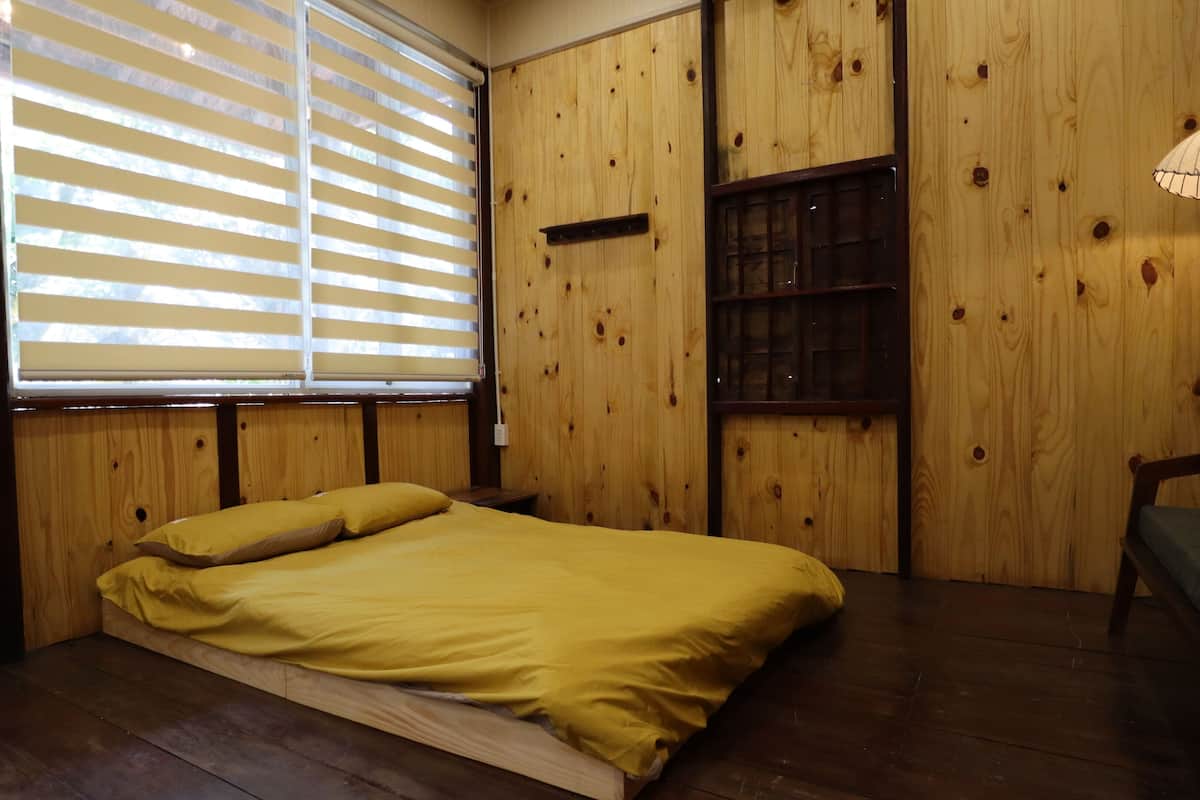 Una habitación con una cama de madera, una ventana con persianas y un estante pequeño.