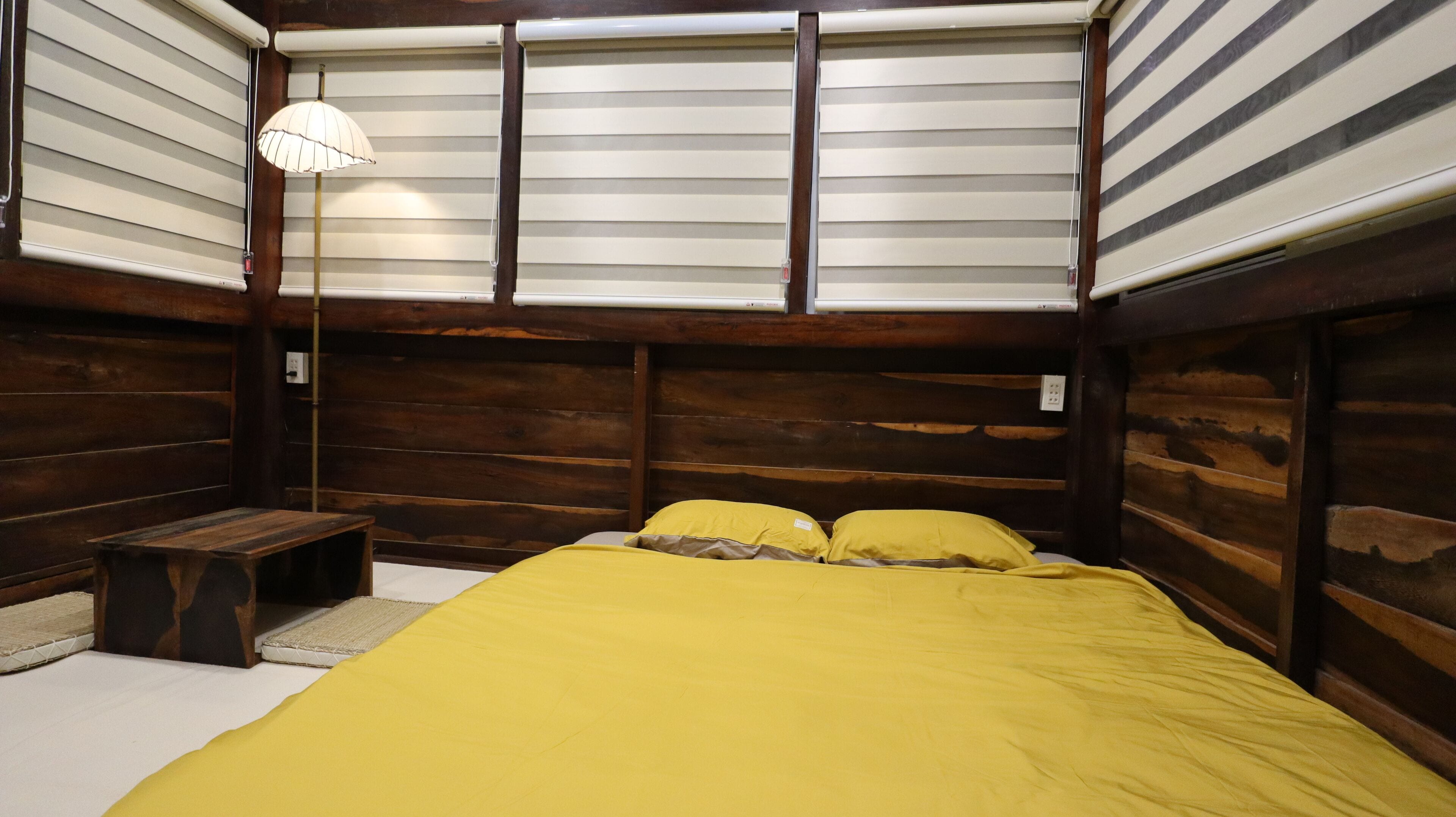 A room with a bed, wooden walls, a bench, and a lamp.