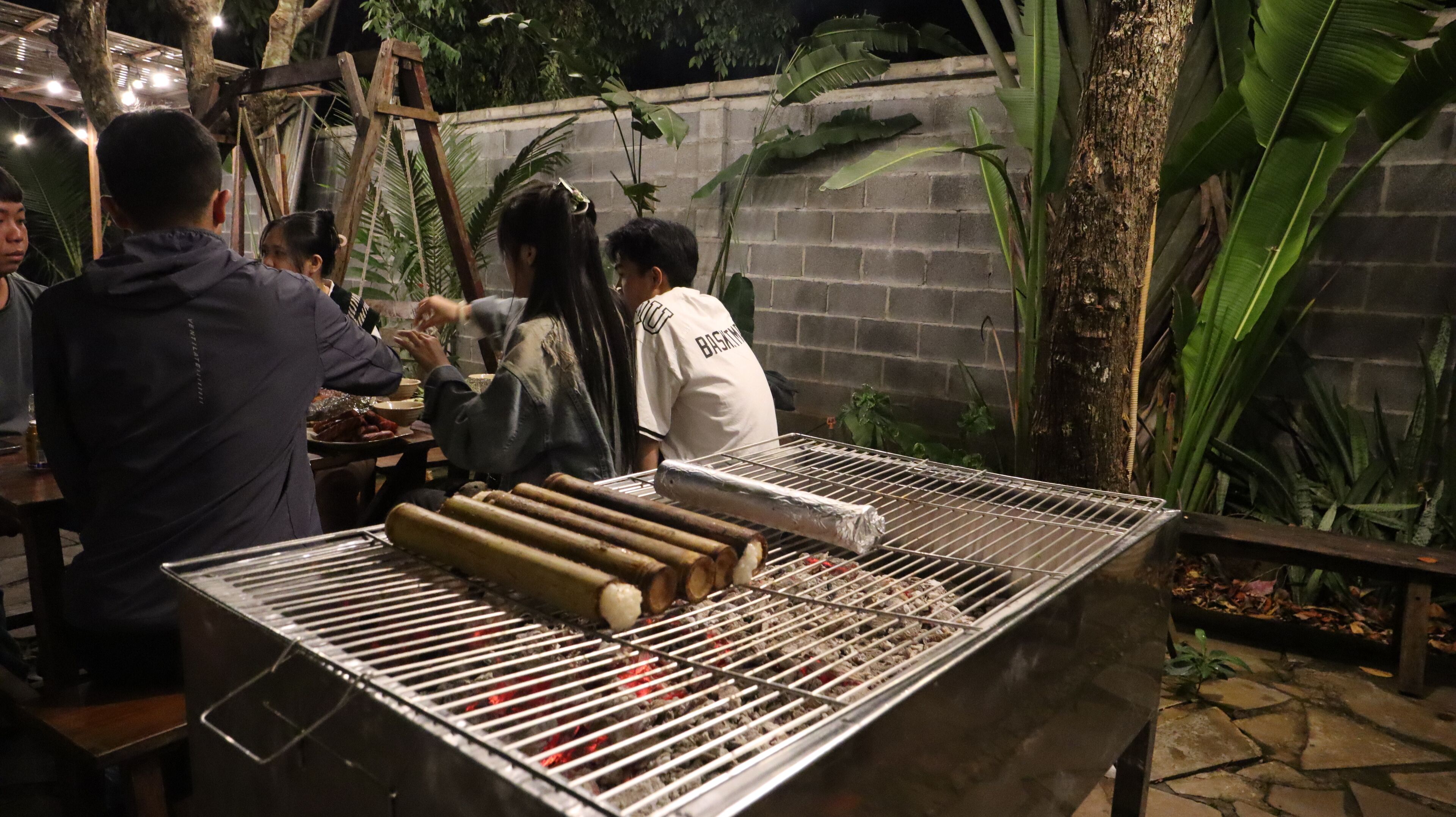 Un groupe de personnes s’est rassemblé autour d’un barbecue où des aliments étaient en train de cuire à l’extérieur, pendant la nuit.
