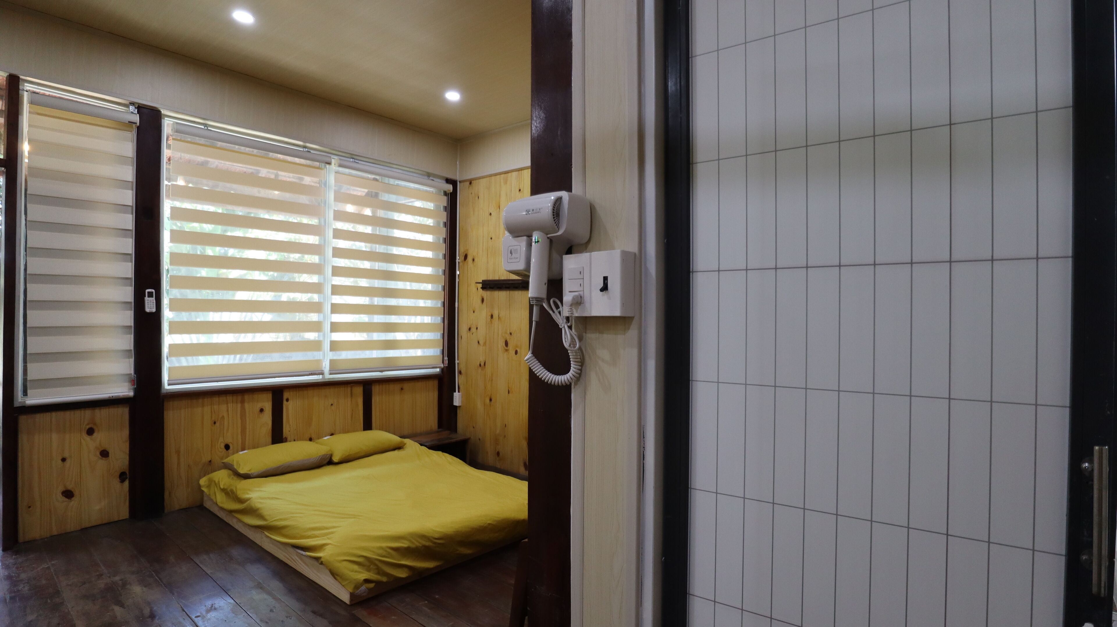 Quarto com cama, paredes de madeira, janela com persianas, secador de cabelo e parede revestida com azulejos.