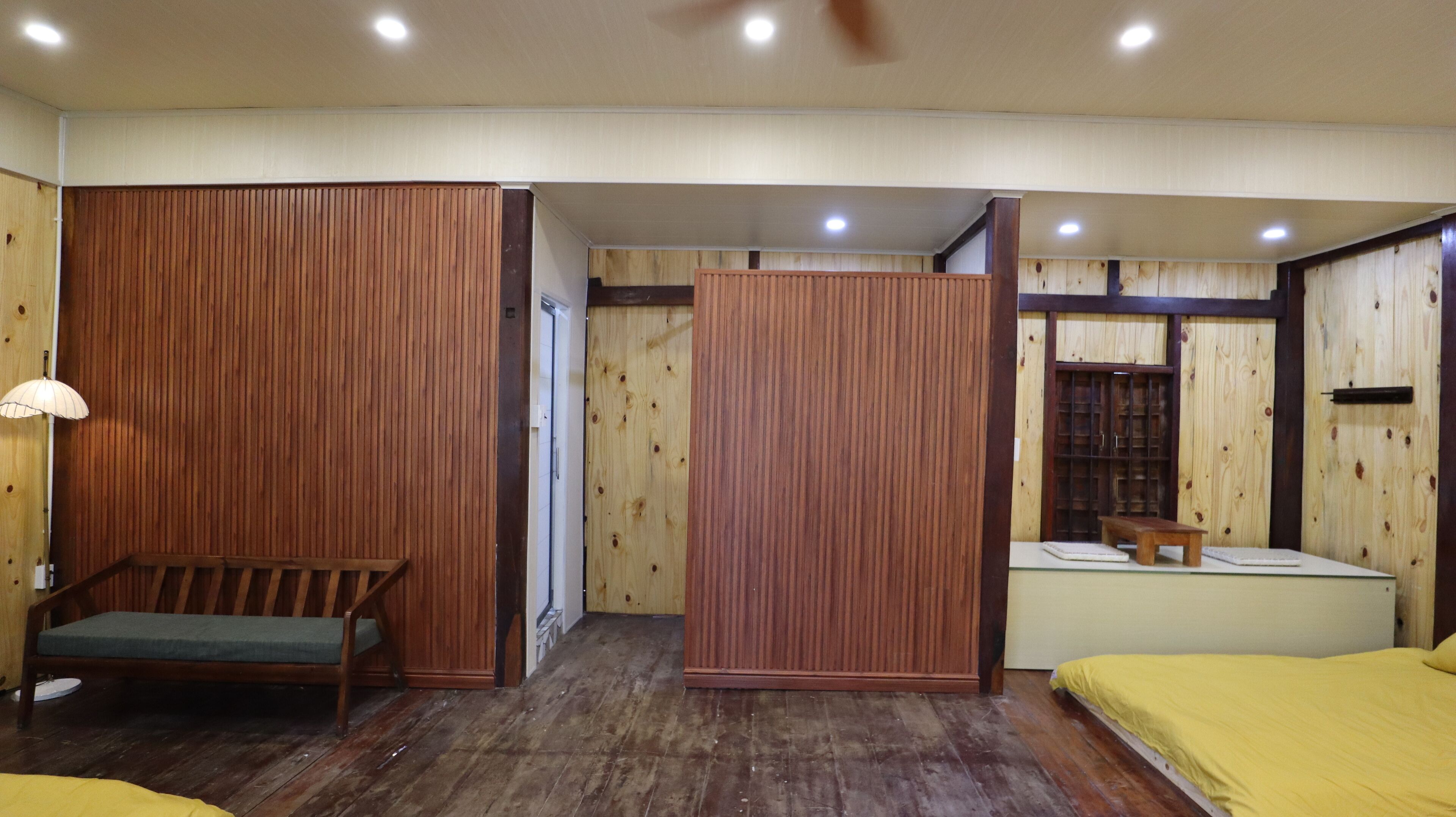 A room with wooden paneling, a bed, a bench, a small table, and a cabinet.