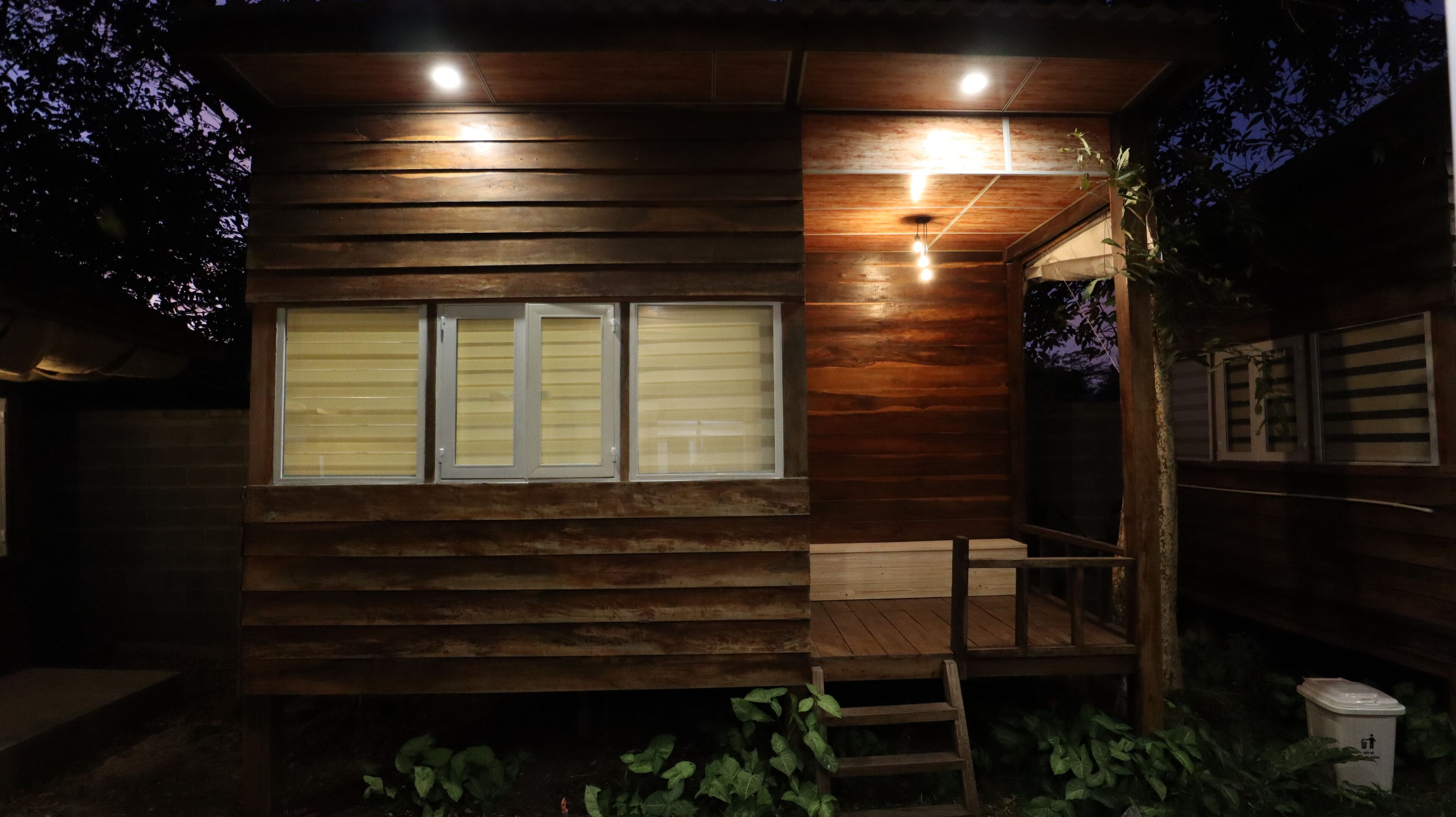 Uma cabana de madeira com três janelas, um alpendre e uma pequena escadaria que leva à porta.