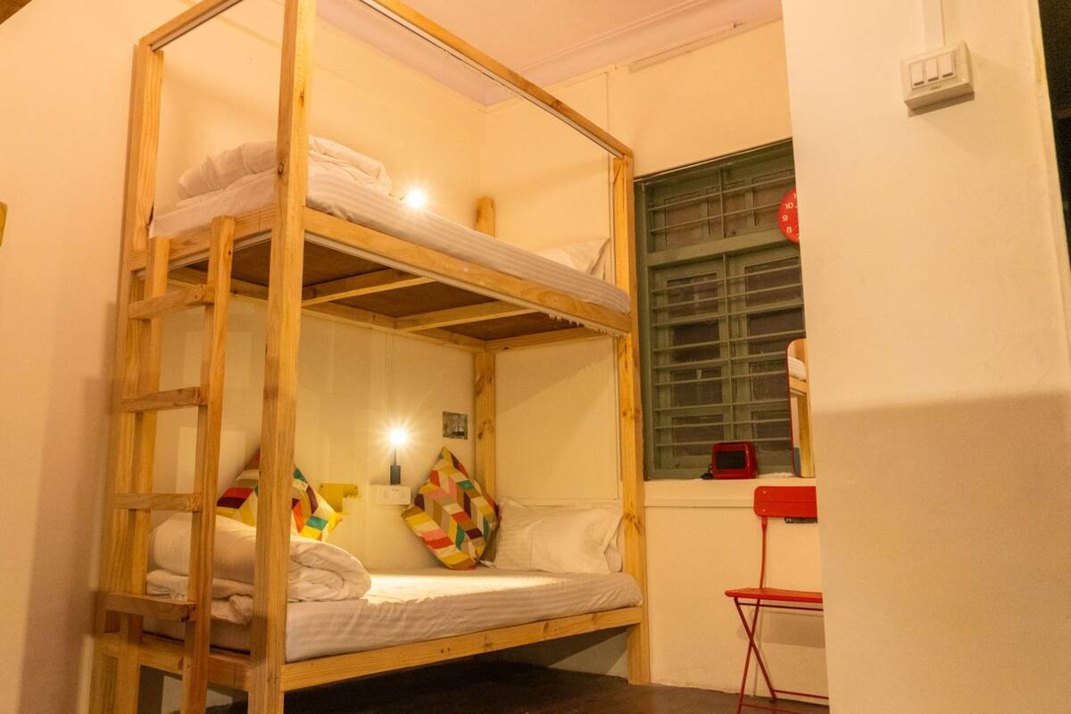 Un lit superposé avec une échelle, une petite table et une fenêtre avec des stores.