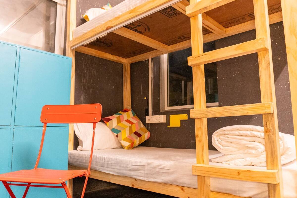 Un lit superposé avec une échelle en bois, une armoire bleue et une chaise rouge.