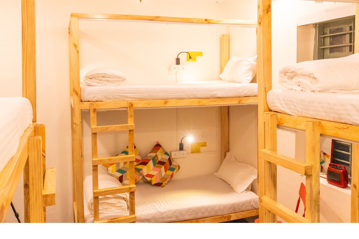 Une chambre avec un lit superposé, une échelle, une petite table et une fenêtre.