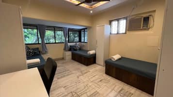 Habitación pequeña con cama, escritorio y silla. Cuenta con ventanas con cortinas, ventilador de techo y aire acondicionado.