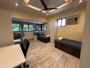 A compact room with a bed, a desk, and a chair. There are windows with curtains, a ceiling fan, and an air conditioning unit. - Locomo Hostel Mini - 9 mins from airport (Mumbai)