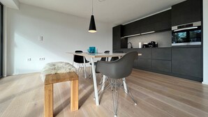 A modern kitchen with dark cabinetry, a wooden dining table, and a black pendant light. - LAKE Loft Azur - in the Überlingen spa district (Überlingen)