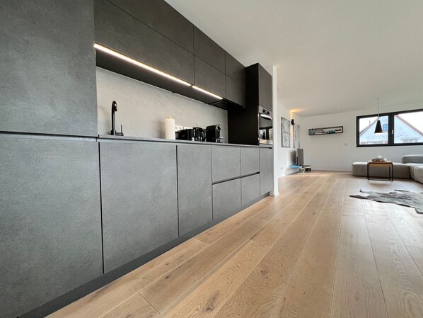 A modern kitchen with grey cabinets, a built-in oven, and a coffee maker.