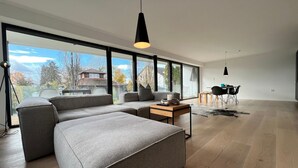 A modern living room with a large sectional sofa, a coffee table, and a dining area with a small table and chairs. - LAKE Loft Azur - in the Überlingen spa district (Überlingen)