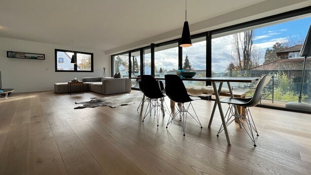 A modern living room with a large window, a dining area with chairs, a sofa, and a coffee table. - LAKE Loft Azur - in the Überlingen spa district (Überlingen)