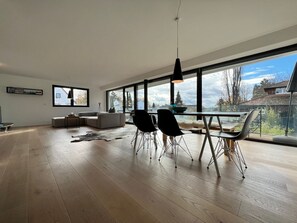 A modern living room with a large window, a dining area with chairs, a sofa, and a coffee table.