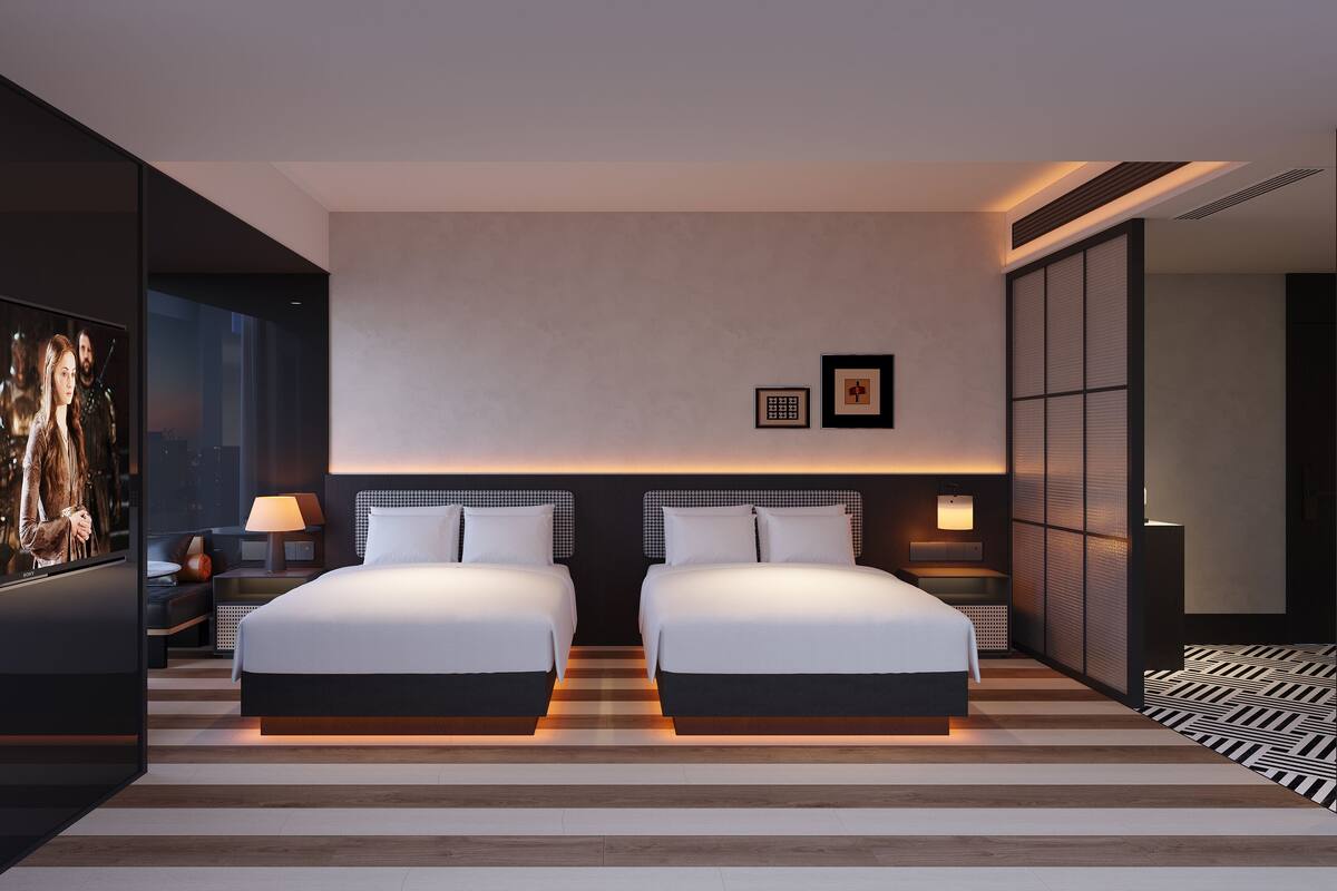 Ein modernes Hotelzimmer mit zwei Betten, einem großen Fernseher und Blick auf die Stadt.