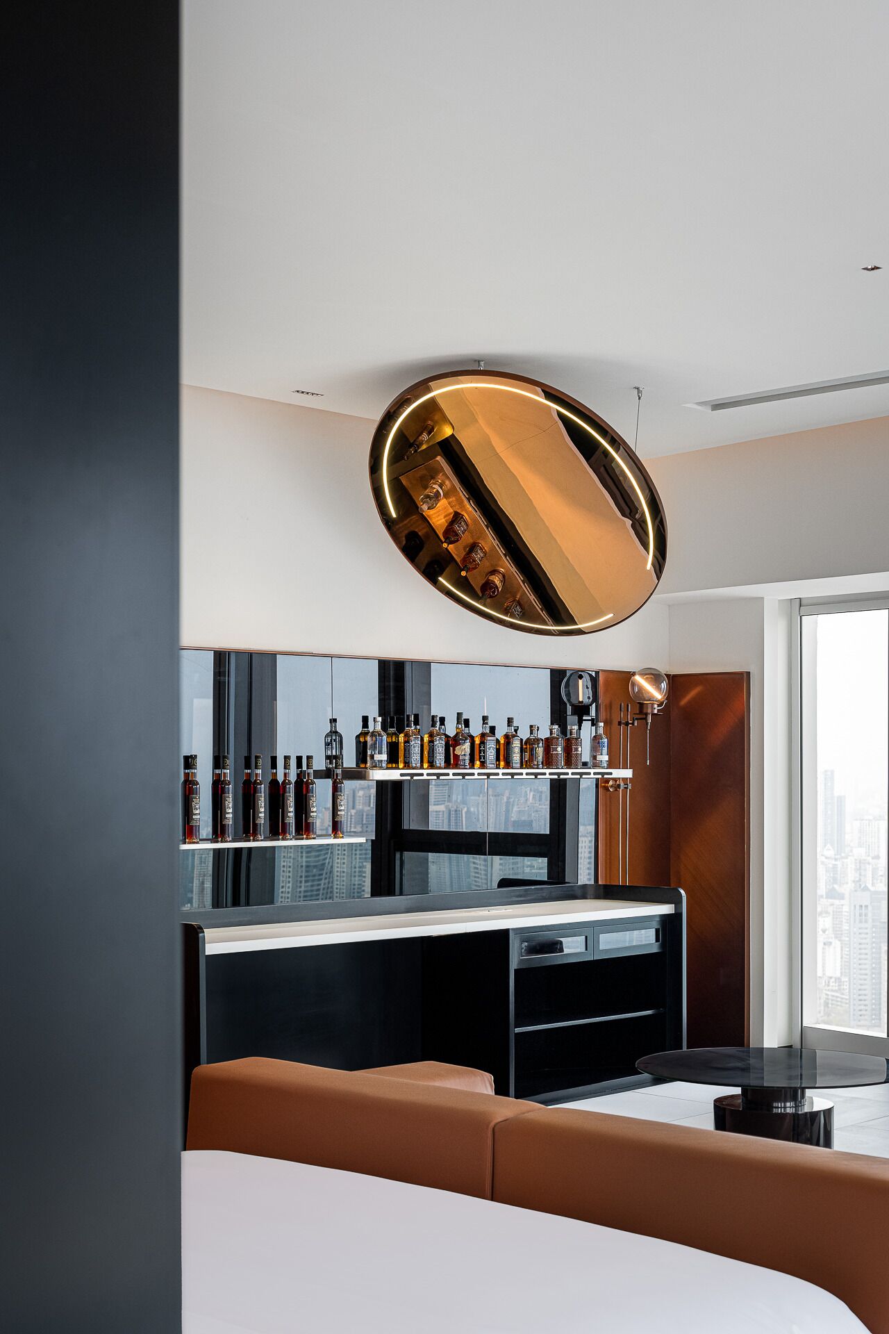 A modern bar area with a mirrored ceiling, a variety of liquor bottles, and a city view through large windows.