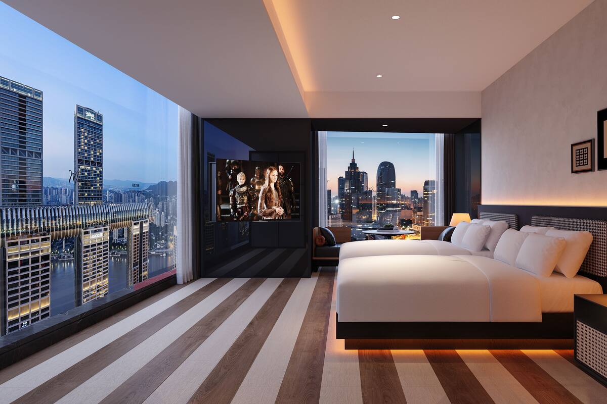 Ein modernes Hotelzimmer mit einem großen Bett, Blick auf die Stadt und einem Fernseher, der eine Sendung zeigt.