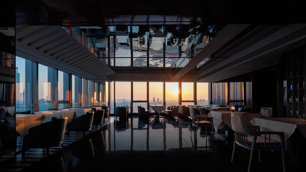 A modern interior with a high ceiling, large windows, and a view of a cityscape at sunset. - Maiyue Hotel-Chongqing Jiefangbei (Chongqing)