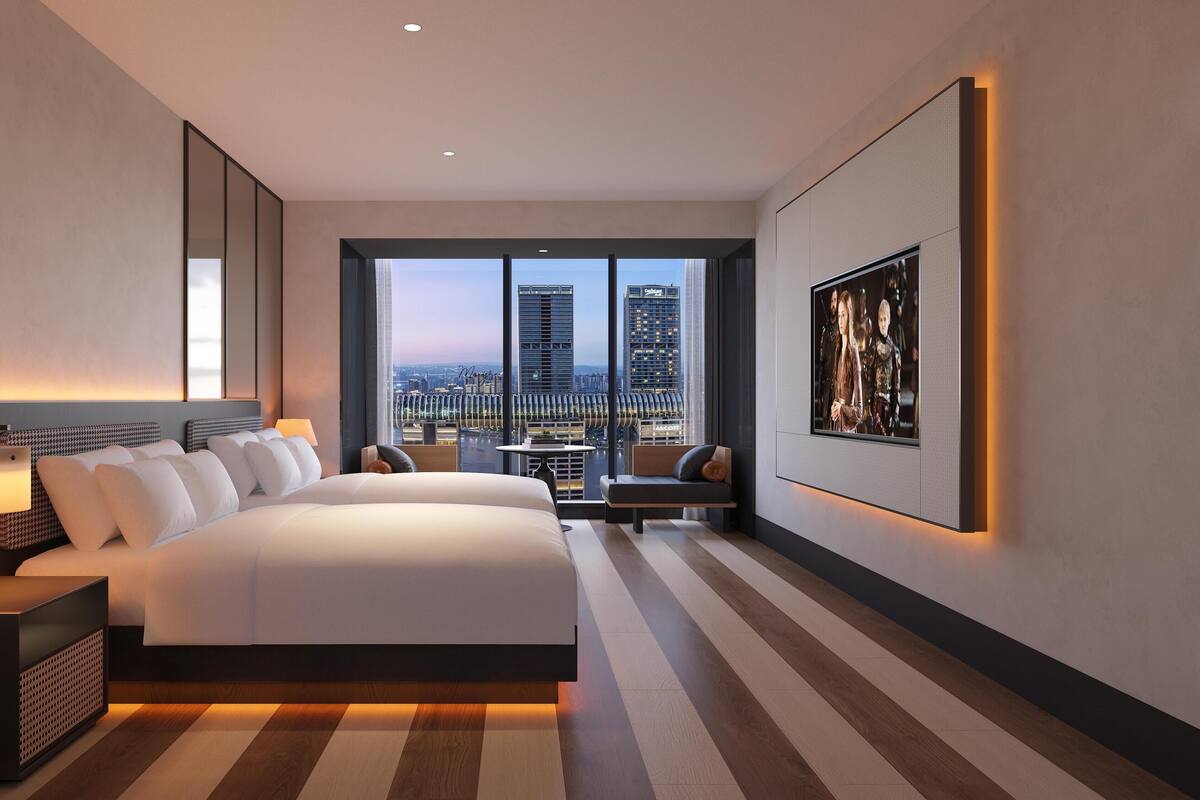 Ein modernes Hotelzimmer mit einem großen Bett, einem Schreibtisch, einem Sessel, einem Fernseher und Blick auf die Stadt.