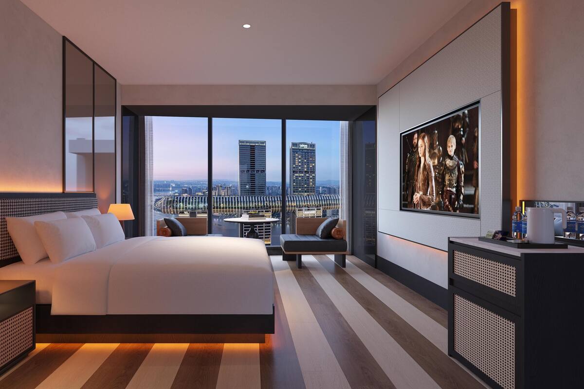 Ein modernes Hotelzimmer mit einem großen Bett, einem Schreibtisch und Blick auf die Stadt.