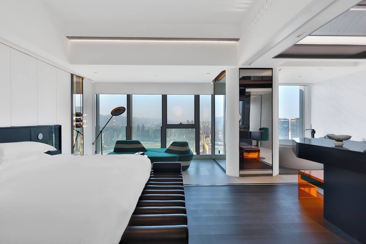 Ein modernes Hotelzimmer mit einem großen Bett, einer Sitzecke und Blick auf die Stadt.