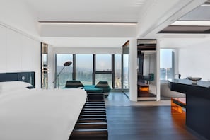 Quarto de hotel moderno com uma cama grande, área de estar e vista para a cidade.