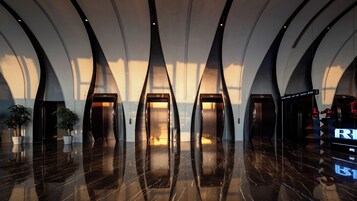 Un vestíbulo moderno con piso de mármol reflectante, varios ascensores y plantas en macetas.
