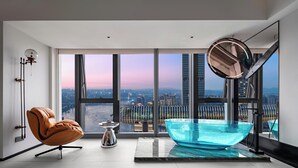 A modern bathroom with a large window, a glass bathtub, a leather chair, and a small table. - Maiyue Hotel-Chongqing Jiefangbei (Chongqing)