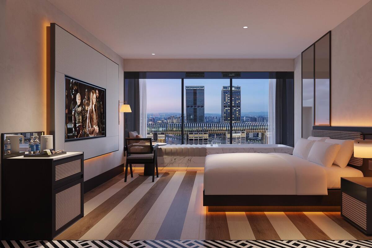 Ein modernes Hotelzimmer mit einem großen Bett, einem Schreibtisch, einem Stuhl und Blick auf die Stadt.
