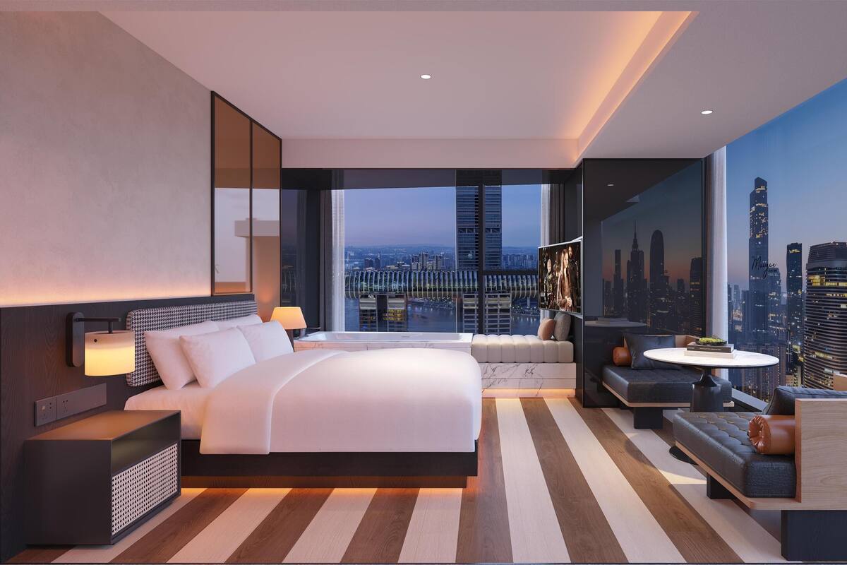 Ein modernes Hotelzimmer mit einem großen Bett, einer Sitzecke, Blick auf die Stadt und einem großen Fenster.