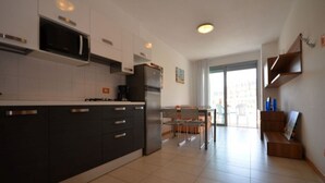 A modern kitchen with dark cabinetry, a built-in microwave, and a refrigerator. There is a dining area with a table and chairs, and a balcony with a view. - Stylish house in the center of Bibione (Bibione)
